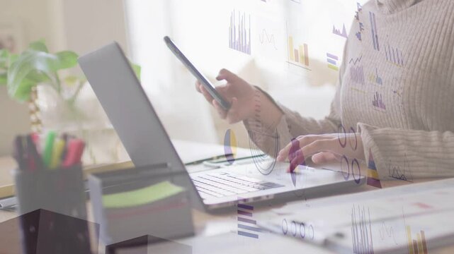 Female professional tapping phone and typing on laptop at desk, producing animated business charts