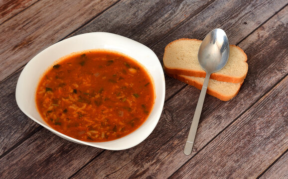 Kharcho, traditional spicy Georgian soup on a wooden table, next to it a tablespoon and two pieces of wheat bread.