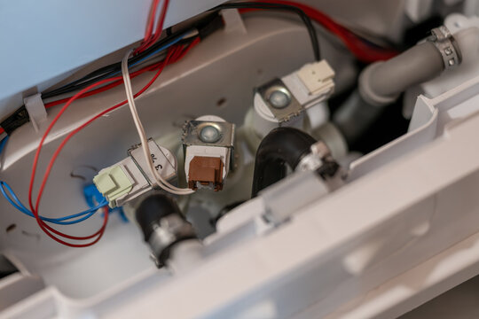 Close-up of water inlet solenoid valves inside an uncovered top-loading washing machine.