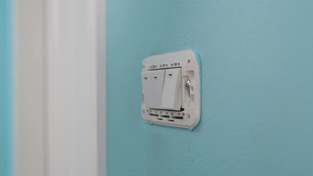 Close-up hand of man wearing cloth gloves and uses a screwdriver to remove a light switch panel for repair.