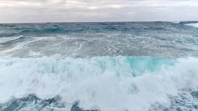 Aerial view of rough sea waves with white foam and choppy water under an overcast sky in Nordland, Norway.