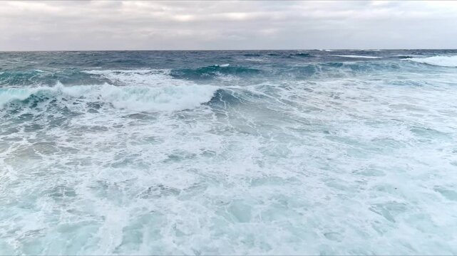Aerial view of rough sea waves with white foam crashing under an overcast sky in Nordland, Norway.