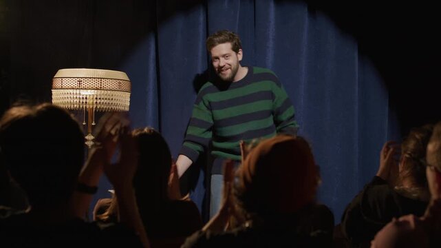 Male comedian walking onto stage, taking microphone, greeting audience and beginning his stand up monologue during performance at comedy club