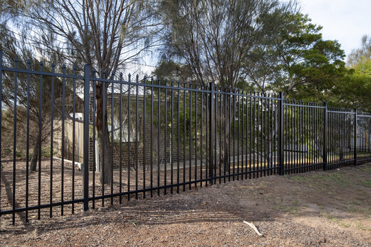 A tall&nbsp;black steel spear top security fence along the perimeter of a suburban property in Australia.&nbsp;&nbsp;Robust metal fencing with vertical steel pickets with pointed spear tops and horizontal rails