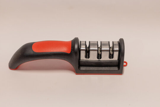 Manual 3-stage knife sharpener with ergonomic red and black handle on white background.