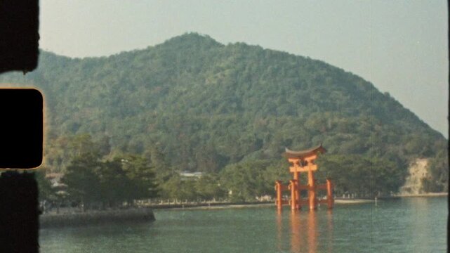 Super 8 mm vintage film of the traditional Itsukushima Shrine temple torii gate in the middle of an ocean bay channel with Mount Misen in the background on Miyajima Island Hatsukaichi Hiroshima Japan