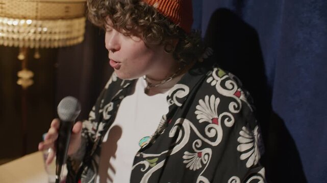 Young female comedian talking into microphone while delivering energetic stand up monologue on stage and entertaining audience at comedy club. Close up shot
