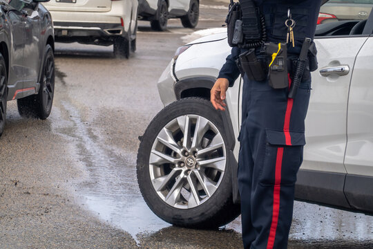 Calgary, Alberta, Canada. April 21, 2026. An RCMP officer investigates a vehicle accident scene with a damaged car on a wet road.