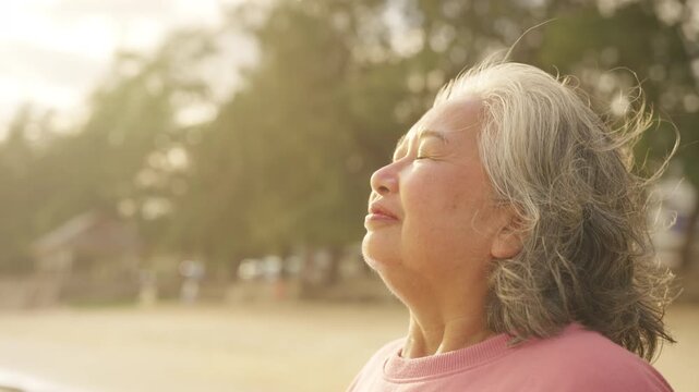 Happy Asian senior woman smiling at beach during sunset, enjoying peaceful moment, active elderly lifestyle, carefree summer holiday vacation, aging gracefully healthy retirement relaxing by seaside.