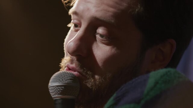 Close up view of emotional stand up performer holding microphone and sharing witty joke during live comedy show on stage