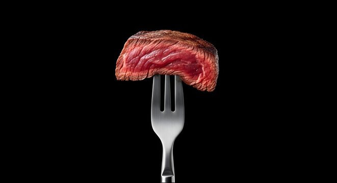 Perfectly cooked medium rare steak slice held up on a silver fork against a stark black background, close up food photography