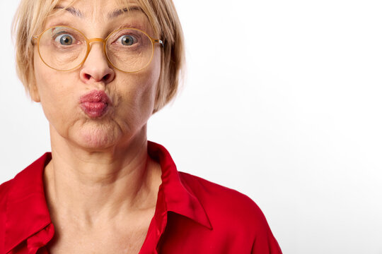 Surprised woman with wide eyes in a red shirt closeup, puckered lips and expression, wearing glasses, studio portrait on white background, showing strong surprise and shock emotion
