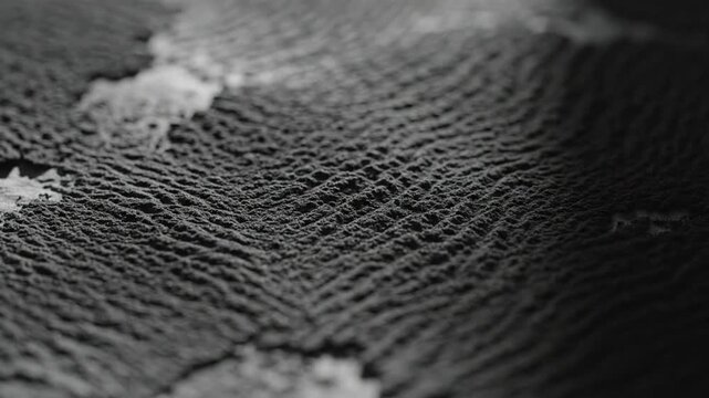 Close-up abstract texture of dark soil with visible granular patterns and subtle light highlights creating a natural
