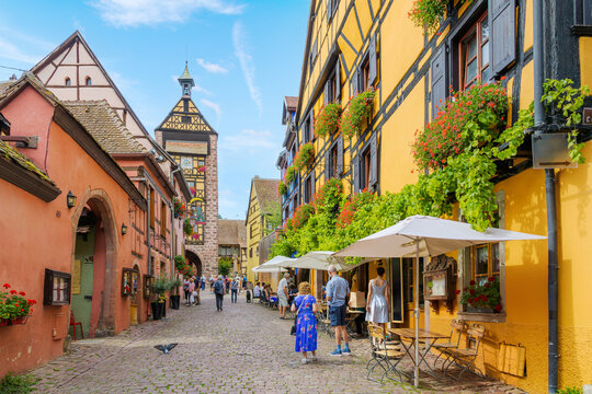 The Dolder Belfry Clock Tower can be seen from a cobblestone street of shops and cafes in the medieval old town of Riquewihr, France, in the Alsace region. 