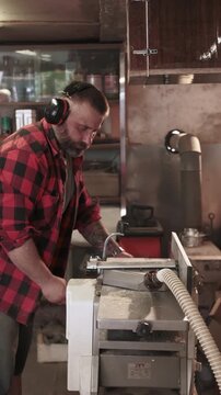 Vertical video. Carpenter work. Furniture making. Man with ear protectors processing wood on thickness planer with dust collection hose.