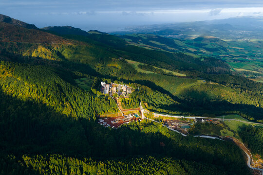 Aerial view of Ribeira Grande Geothermal Power Station surrounded by dense green forests and rolling hills under a soft morning light Ribeira Grande, Acores, Portugal.