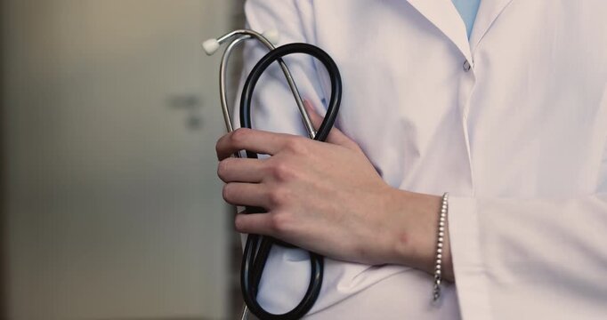 Closeup cropped view unknown female doctor wearing white coat, holding stethoscope, represents health checkup, cardiology services, healthcare profession, medical care, diagnostic practice in clinic
