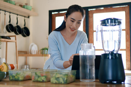 Woman using tablet to follow healthy cooking recipe while preparing fresh meal at home kitchen