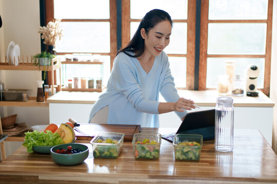 Woman using tablet to follow healthy cooking recipe while preparing fresh meal at home kitchen