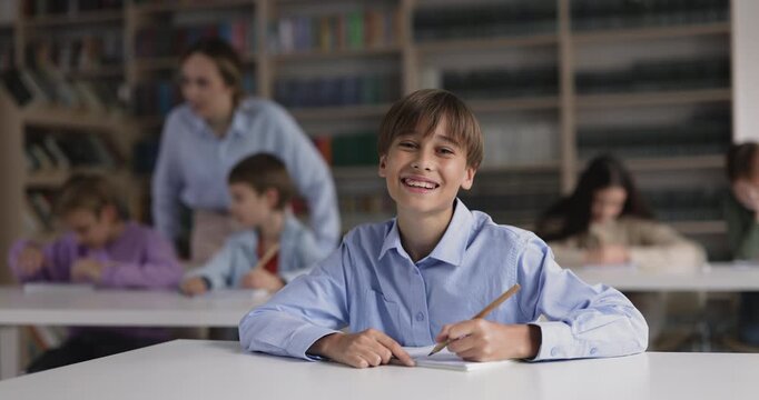 Portrait of smiling schoolboy writing in copybook, making schoolwork in classroom during class at school desk. Primary school education, studying process, gaining new knowledge, skills improvement
