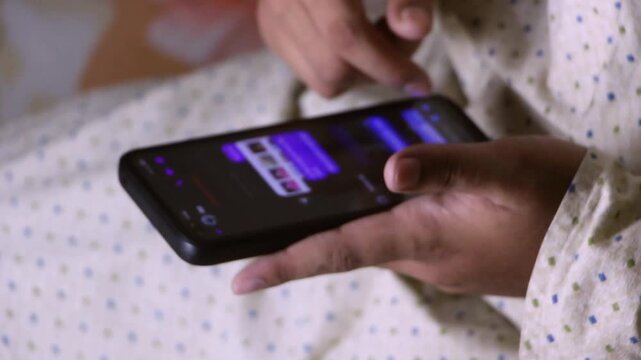 Close-up of hands holding a smartphone in landscape mode and swiping the touchscreen while relaxing indoors. Using their index finger to swipe, scroll, and tap across the glowing touchscreen.