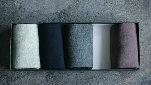 Male hand picking one pair of warm, dark colored socks from a neatly organized box on a gray concrete background, showcasing a selection of new hosiery and the concept of making a choice