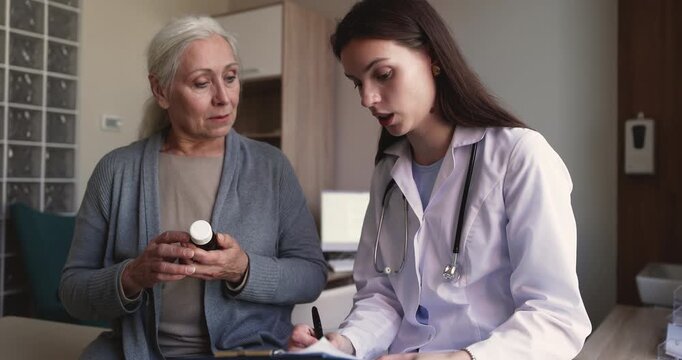 Female doctor holding pills bottle, explaining medication instructions, describing dosage of prescribed medicine to senior patient during medical visit in clinic. Treatment plan, healthcare services