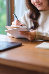 Naklejka premium Vertical closeup image of a woman writing on a notebook while working on laptop computer at home