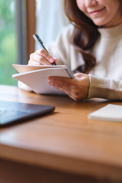 Vertical closeup image of a woman writing on a notebook while working on laptop computer at home