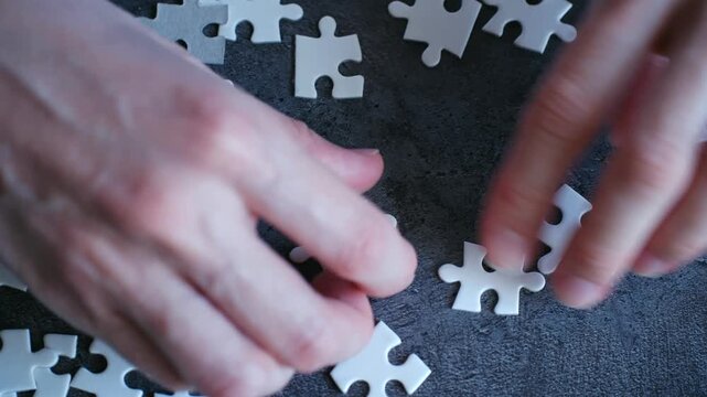 Close up hands assembling blank white jigsaw puzzle, symbolizing problem solving, strategy, teamwork. Business concept for finding solution, achieving success together. Hands connecting puzzle pieces.