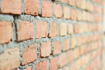 Fototapeta premium Side view of an unfinished red brick wall with selective focus. Rough clay bricks and grey mortar texture. Industrial background for construction or architecture projects.
