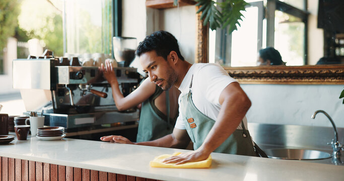 Cleaning, cloth and counter with man in coffee shop for maintenance of small business startup. Hospitality, hygiene and wipe with people in restaurant cafe to disinfect surface for sanitizing routine