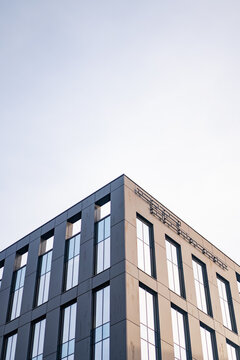 The sharp corner of a modern office building features dark gray cladding and large glass windows. This low-angle shot emphasizes the clean lines of contemporary urban architecture.
