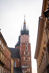 Obraz premium Gothic brick tower of St Marys Basilica rises between historical European buildings in Krakow. Low angle view represents ancient architecture and cultural heritage tourism.