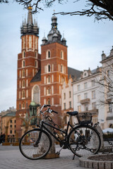 Fototapeta premium A classic black city bicycle parked on a stone square, with the historic St. Mary's Basilica and old town architecture of Krakow, Poland, softly blurred in the background.