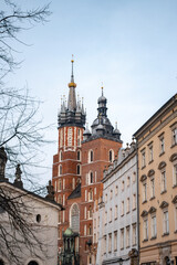 Obraz premium Vertical view of the iconic Gothic towers of St. Mary's Basilica rising above the historic architecture of Krakow's Old Town square under a clear, soft morning sky in Poland.