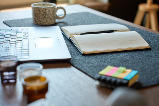 Laptop and open notebook with pen on desk in home office interior with coffee mug and sticky notes. Concept of planning, productivity, remote work and study.