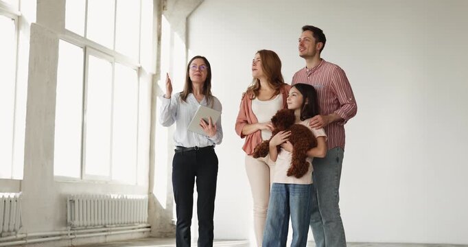 Real estate agent showing empty apartment to family with child and dog, standing in unfurnished living room, talking, discussing house features, viewing property for rent or buy. Relocation, bank loan