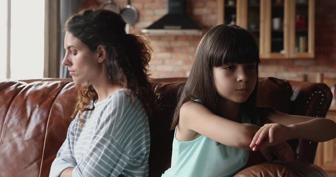 Sulking mother and daughter sitting together on couch at home, looking sad and emotionally distant, showing frustration. Family conflicts, communication issues, parenting challenges, misunderstanding