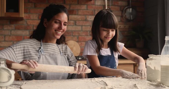 Mother teaching her child daughter making dough for homemade pastry in kitchen at home, family having fun, enjoying happy moments during food preparation. Learning culinary skills, knowledge sharing