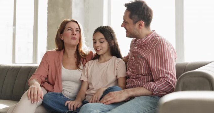 Couple talking to daughter sitting on couch in living room, family leading casual conversation, spending leisure time together at home. Communication, trust and understanding between parents and child