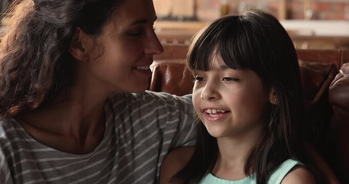 Closeup adult mother whispering secret to daughter, sharing fun, laughing, enjoying moment of family bonding and connection. Concept of trust between parent and child, communication, relationships
