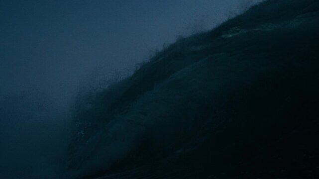 Dark ocean wave wall rising dramatically with deep blue water and textured crest at sea level, slow motion backdrop