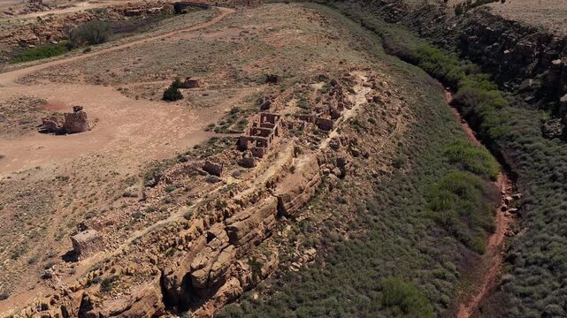 A drone following shot tracks along the rim of a canyon, passing by ruined stone walls and abandoned structures. This footage is ideal for narrative b-roll focused on the history of the Southwest.