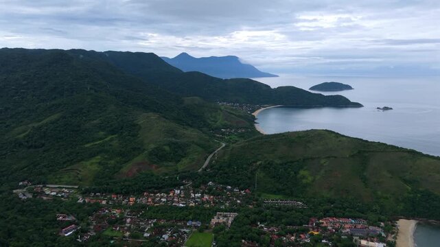 Rural town of Maresias, Atlantic ocean and lush green hills on a cloudy tropical day in S&atilde;o Paulo. High forward aerial pass.