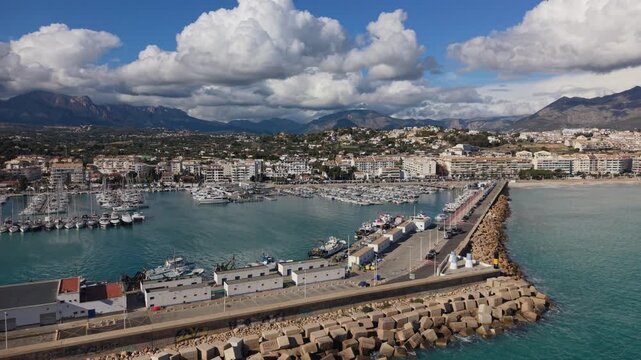 Albir and Altea Costa Blanca Spain.Reveal of seawall,harbour and marina out to sea over calm blue water with backdrop of buildings, mountains and interesting clouds in bright sun