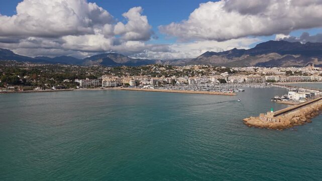 Albir and Altea Costa Blanca Spain.Circling and Panning drone footage of harbour entrance and marina over calm blue water,boat coming into port with backdrop mountains and clouds in bright sun