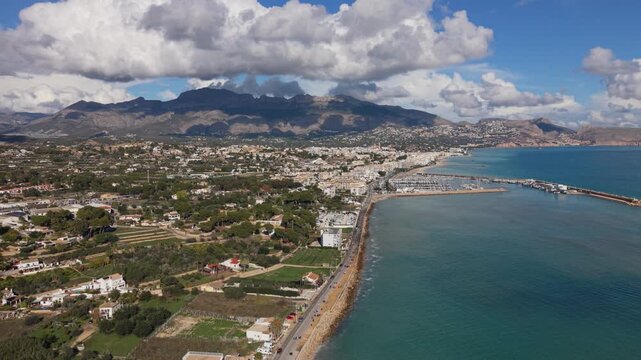 Albir and Altea Costa Blanca Spain.High backwards drone footage of seafront of both resorts with harbour and marina over calm blue water and backdrop of mountains and interesting clouds in bright sun