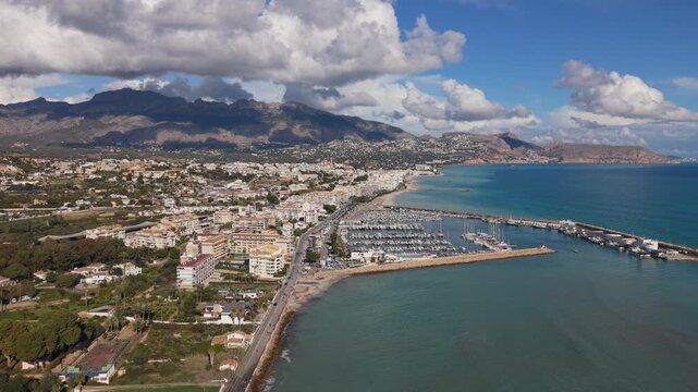 Albir and Altea Costa Blanca Spain.High drone footage over marina and seafront with calm blue water and backdrop of mountains and interesting clouds in bright sun