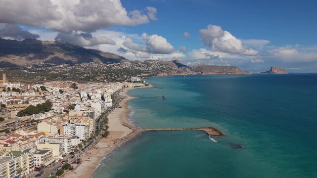 Albir and Altea Costa Blanca Spain.Drone flying along beach and seafront and dropping down to crystal clear blue water with backdrop of mountains and interesting clouds in bright sunshine